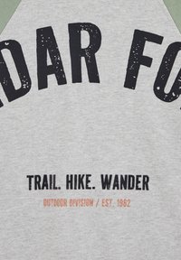 Tissu gris avec texte noir "TRAIL. HIKE. WANDER" et texte orange délavé "OUTDOOR DIVISION / EST. 1962" sous de grandes lettres noires partielles.