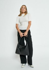 Bolso de hombro de cuero negro con una forma suelta, combinado con una blusa blanca ajustada y pantalones negros. Textura suave destacada y diseño minimalista.