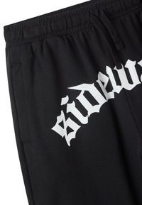 Pantaloni sportivi neri con finitura testurizzata, caratterizzati da una stampa grafica bianca con la scritta "side" sulla gamba sinistra e una vita elastica con lacci.