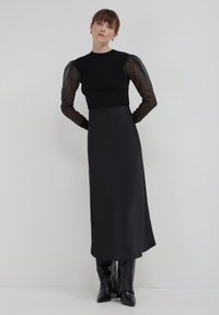 Abito nero con un corpino aderente e maniche lunghe trasparenti. Tessuto liscio e opaco con una gonna dritta. Stivali neri al ginocchio completano il look.