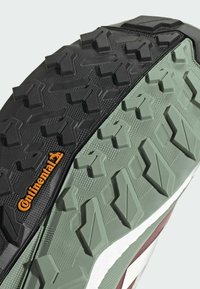 Kenkäpohja, jossa on musta ja vihreä kumipohja, jossa on kulmikkaita kuvioita ja Continental-logo oranssilla. Teksturoitu pidon ja kestävyyden takaamiseksi.