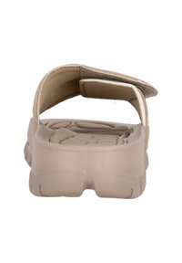 Beige slip-on sandal med bakrem, vadderad sula och texturerad fotbädd. Har en mjuk tygfoder och en enkel design.