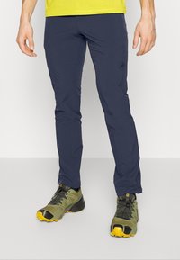 Pantalons légers marine avec une coupe slim, fabriqués à partir d'un tissu extensible. Assortis à des chaussures de trail vertes et jaunes avec des semelles de traction.