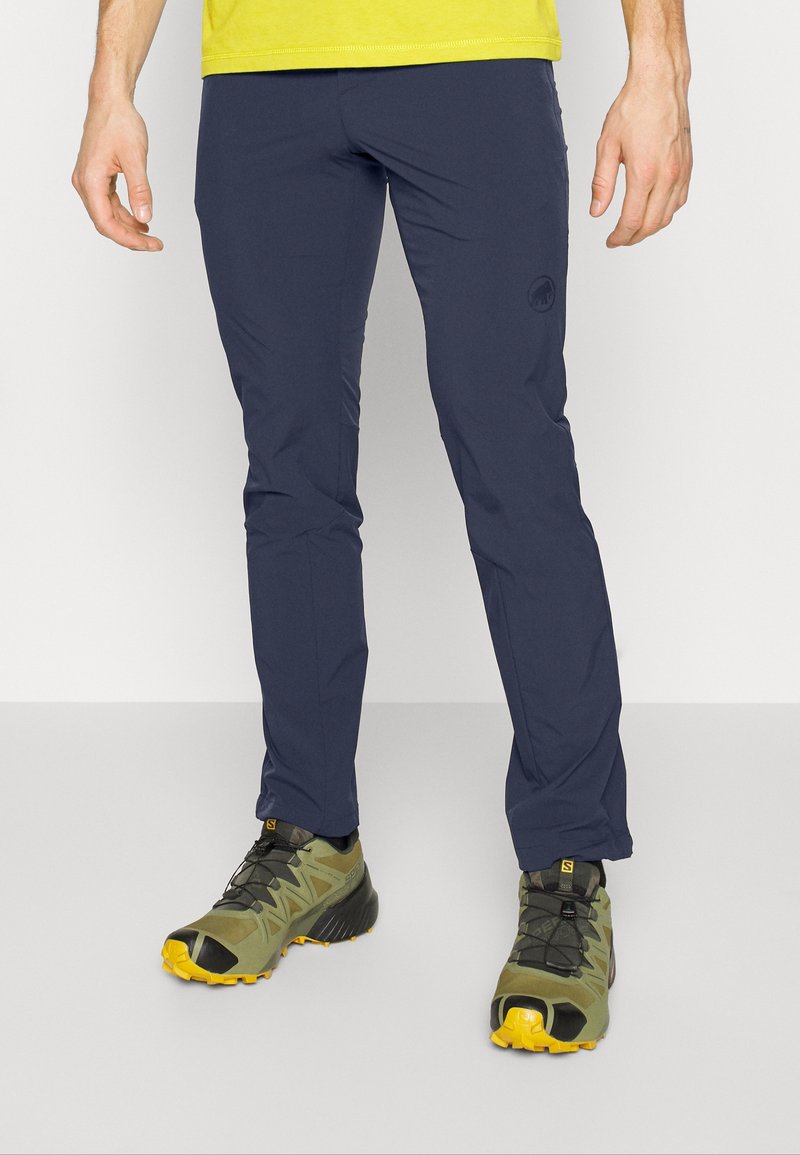 Pantalons légers marine avec une coupe slim, fabriqués à partir d'un tissu extensible. Assortis à des chaussures de trail vertes et jaunes avec des semelles de traction.