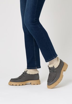 Stivaletti in pelle grigia con suole in gomma beige, caratterizzati da un colletto bianco soffice. Indossati con jeans scuri e calzini color crema.