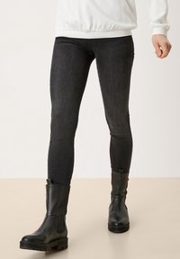 Leggings de mezclilla negra con un corte ajustado, combinados con botines de cuero negro; acabado texturizado notable y suelas de goma resistentes.