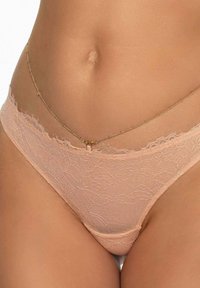 Koronkowy string w delikatnym brzoskwiniowym kolorze, z falbaniastymi krawędziami, z akcentem w postaci złotego łańcuszka łączącego pas i boki dla dodatkowego detalu.