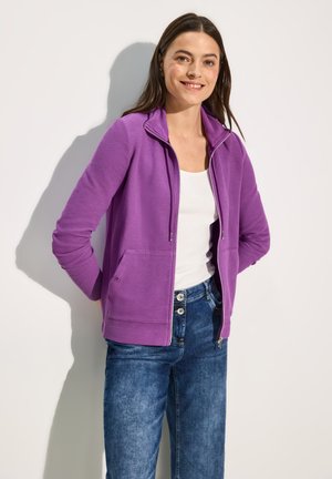 Purple zip-up jacket with a hood, featuring a textured fabric, two front pockets, worn over a white top and blue denim jeans.