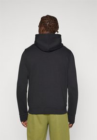 Haut à capuche noir avec une capuche superposée, fabriqué en tissu doux. Le design présente des poignets et un ourlet côtelés, associé à un pantalon de survêtement vert clair.