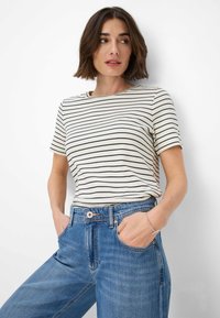 T-shirt bianco con strisce orizzontali nere, maniche corte e collo rotondo, abbinato a jeans di denim blu a vita alta.