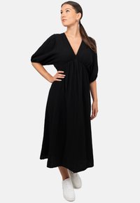 Abito midi nero realizzato in tessuto testurizzato con scollo a V, maniche a sbuffo e vita arricciata. Abbinato a scarpe da ginnastica bianche.