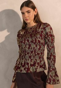 Burgundi peplum pluus metallilise kuldse lillemustriga, voltidega rinnaosa ja kellukeste vars külluslikud. Sile, õhuline kangas.