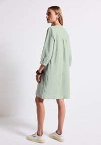 Robe vert clair, longueur genou, à manches trois-quarts, coupe ample, dos froncé et tissu texturé ; assortie à des baskets blanches.