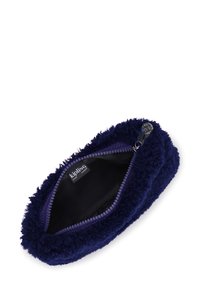 Pequeño estuche de terciopelo azul marino con cremallera abierta que muestra un interior negro y una etiqueta de la marca Kipling en el interior.