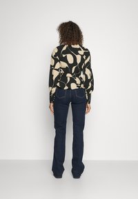 Blusa a maniche lunghe nera e beige con motivo a fantasia e vita legata, abbinata a jeans a zampa d'elefante blu scuro. Tessuto morbido e vestibilità strutturata.
