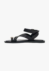 Zwarte platte sandalen met een kruisriemontwerp, voorzien van een glanzende gouden accent op de teenlus en een duurzame rubberen zool. Gladde textuur.