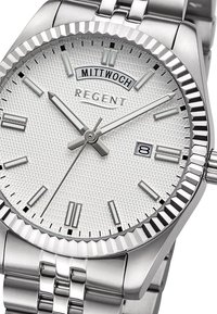 Montre en acier inoxydable avec un cadran argenté texturé, une lunette striée et un indicateur de date. Comprend des marqueurs d'heure et des aiguilles argentés.