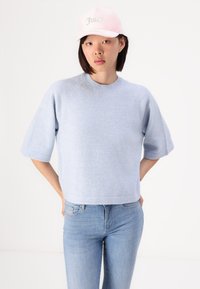 Lyseblå kortermet genser med en myk tekstur, rund hals og lett crop design, kombinert med en rosa caps med rhinestone-bokstaver.