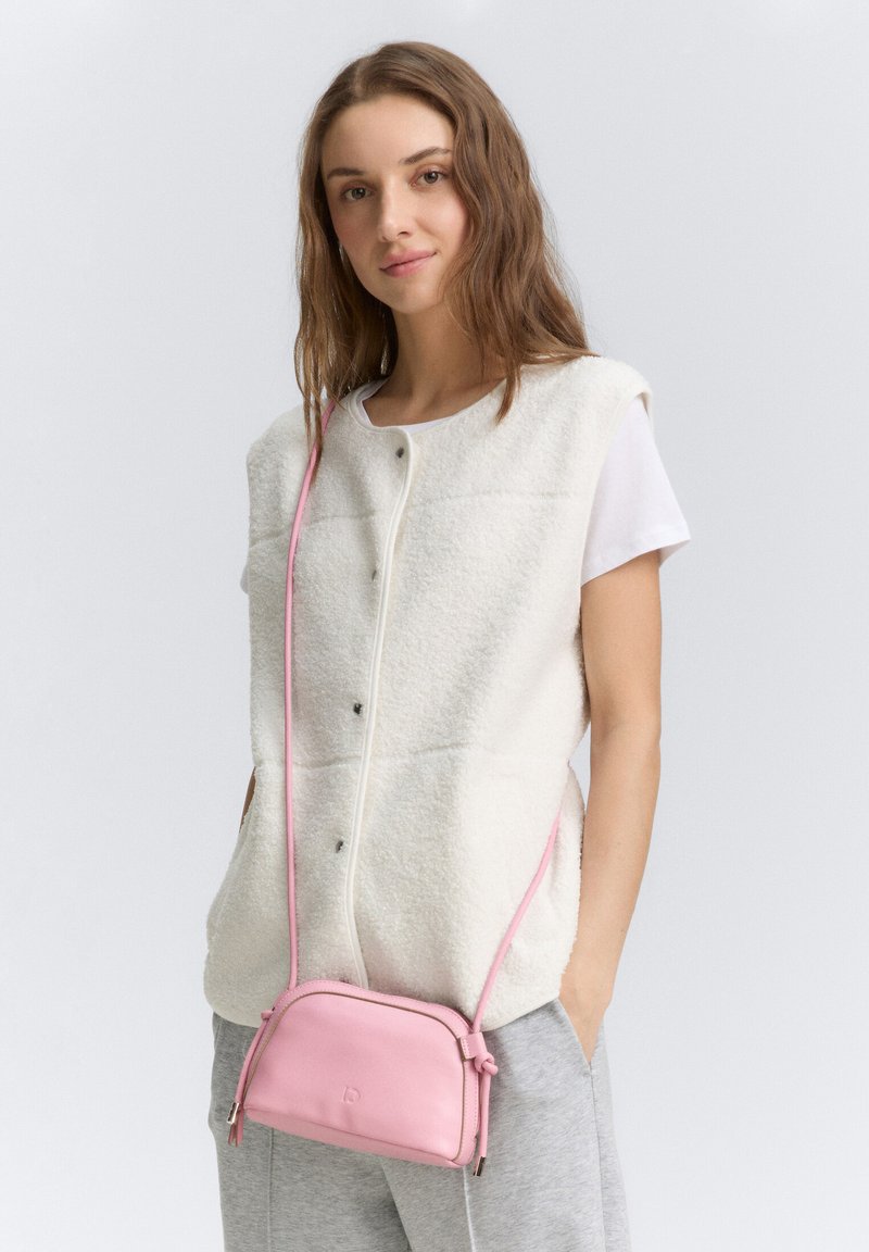 Gilet di pile bianco con scollatura rotonda e bottoni a pressione, abbinato a una piccola borsa a tracolla in pelle rosa. I pantaloni grigi completano l'outfit.