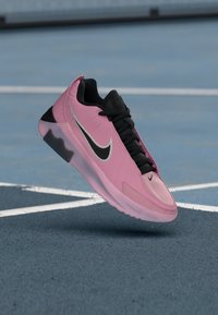 Rosa treningssko med svarte detaljer, som har en teksturert overdel, tykk såle og en fremtredende sølvfarget Nike-swoosh.