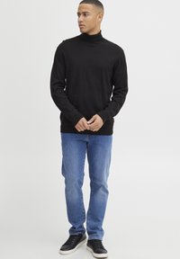 Zwarte coltrui met lange mouwen, gemaakt van een zacht materiaal. Gepaarde met lichtblauwe spijkerbroek en zwarte sneakers. Eenvoudig, aansluitend ontwerp.