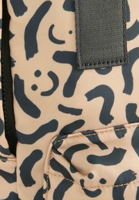 Beige stofpose med mørkeblå abstrakte mønstre. Har en frontlomme med sort lynlås og tekstureret syning. Enkle stropper vises.