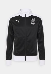 Black zip-up jacket made of smooth fabric, featuring white shoulder and wrist accents, a high collar, and embossed team logo on the chest.