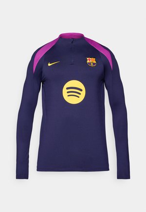 Vijolična in mornarsko modra dolga majica iz jersija z zadrgo pri ovratniku, ki na prsih nosi rumeni logotip Spotify in grb Barcelone. Prisoten je tudi Nikeov znak.