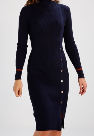 Navy blue ribbed knit midi dress with long sleeves, turtleneck, red stripe on cuffs, and buttons running asymmetrically from waist to hem.