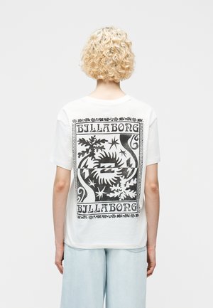 Inimene lokkis blondide juustega, kandes valget Billabongi T-särki, millel on must abstraktne päikese- ja lehemuster, ning helesiniseid pükse.