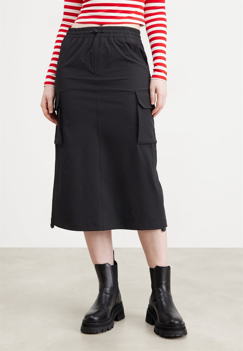 Sort midi-nederdel lavet af letvægtsstof, med elastik i taljen og to store sidelommer. Glat tekstur med en lige snit.