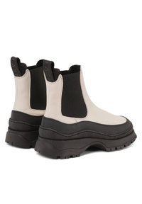 Chunky Chelsea boots in cream and black, featuring smooth leather, elastic side panels, and thick rubber soles with deep treads.