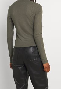 Maglia a maniche lunghe a coste color oliva abbinata a pantaloni neri in ecopelle a vita alta, con tasche posteriori e una finitura liscia.