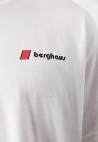 Hvit bomull T-skjorte med en svart "berghaus" logo og et rødt kvadrat som aksent. Glatt tekstur, kort ermer, standard passform.