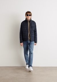 Juodas siuvinėtas švarkas su aukštu apykakle, vilkimas ant rudos golfinės megztinio, derinamas su šviesiai mėlynomis džinsomis ir baltais sportbačiais. Aksesuarai - juodi saulės akiniai.