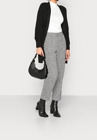 Černý pletený kardigan, bílý rolák, kostkované šedé kalhoty, černá kabelka a černé kotníkové boty na podpatku. Texturovaná látka a střih na míru.