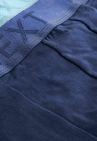 Banda vita blu navy con dettagli testurizzati, con la scritta "NXT" in rilievo. Tessuto morbido con una consistenza liscia, design parzialmente arricciato.