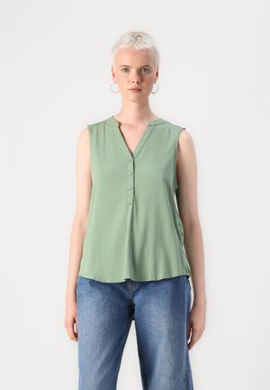Light green sleeveless blouse with a V-neck, button placket, and soft, smooth fabric. Worn with loose denim jeans, casual fit.