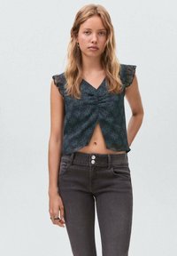 Blusa con stampa floreale scura, maniche corte a volants, scollatura a V, davanti arricciato e lunghezza cropped. Indossata con jeans scuri a vita alta.