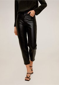 Pantalons en similicuir noir avec une finition texturée, dotés d'une taille haute, de jambes droites et d'un ourlet court, associés à des sandales noires à lanières.