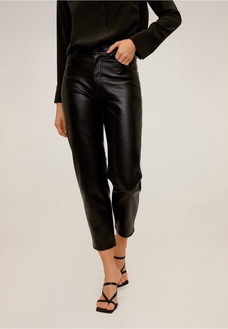 Pantalons en similicuir noir avec une finition texturée, dotés d'une taille haute, de jambes droites et d'un ourlet court, associés à des sandales noires à lanières.