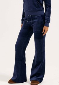 Pantalon de survêtement en velours bleu marine avec un design évasé, deux poches avant, une taille à cordon et une finition douce et texturée.