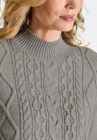 Grauer gestrickter Pullover mit hohem Rippkragen und einem strukturierten Kabelmuster auf der Vorderseite. Weiches, mittelschweres Material.