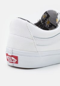 Vit Vans-sneakerhälen med röd "Off The Wall"-logotyp, kanvasmaterial och synlig innerfoder med prästkrage-mönster.