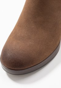 Brązowe zamszowe botki za kostkę z okrągłym noskiem i ciemną, drewnopodobną podeszwą platformową, o gładkiej powierzchni i minimalnych detalach szwów.