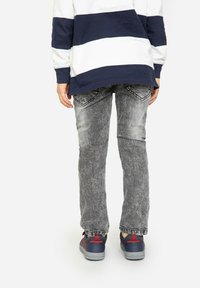 Jean en denim gris avec une texture usée, design taille mi-haute, et détails de poche arrière, associés à des baskets navy avec des accents rouges.