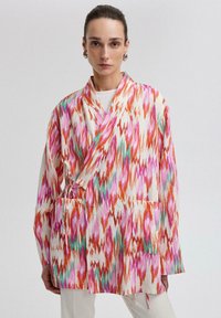 Barevná, vzorovaná kimono bunda z lehkého materiálu, zdobená oranžovými, růžovými a zelenými cik-cak vzory. Obsahuje boční kapsy a zavírání na šňůrku.
