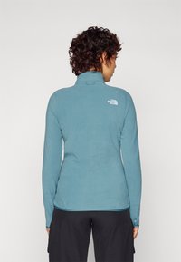 Heledad sinine fliisist pullover kõrge kaelusega, pikad varrukad ja väike logo ülalt taga. Pehme tekstuur, liibuv disain ja nööbid varrukaotsadel.