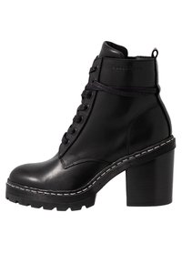 Svart läderankelboot med chunky klack, snörningsdesign och vit sömdetalj längs sulan. Har en rund tå och robust konstruktion.