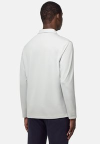 Witte polo met lange mouwen en een zachte textuur, voorzien van een klassieke kraag. De achterzijde heeft een strakke uitstraling en minimaal stiksel.